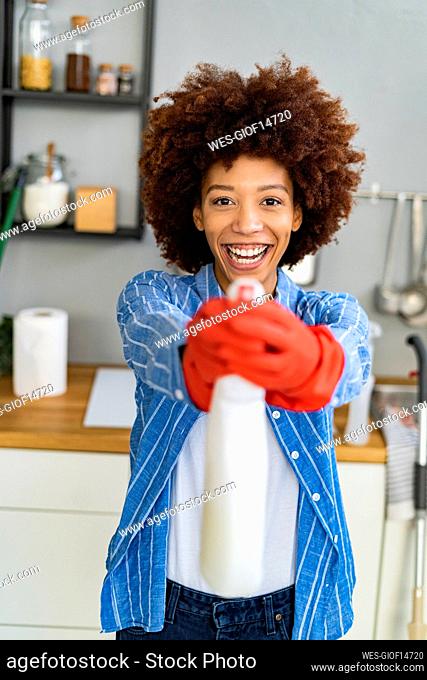 Cheerful young Afro woman holding disinfection spray bottle in kitchen
