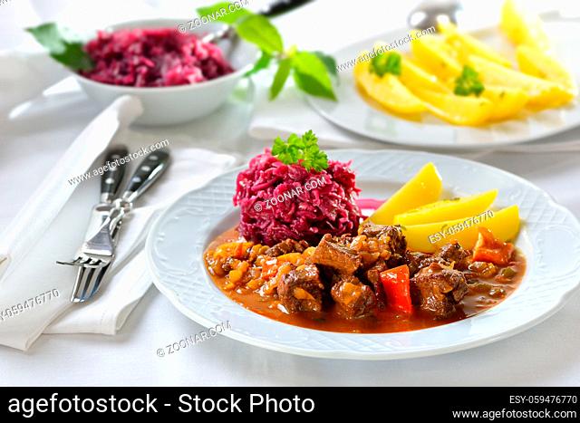 Deftige Hausmannskost: Pikantes ungarisches Gulasch mit Petersilienkartoffeln und Rotkraut serviert ? Hot Hungarian goulash served with parsley potatoes and red...