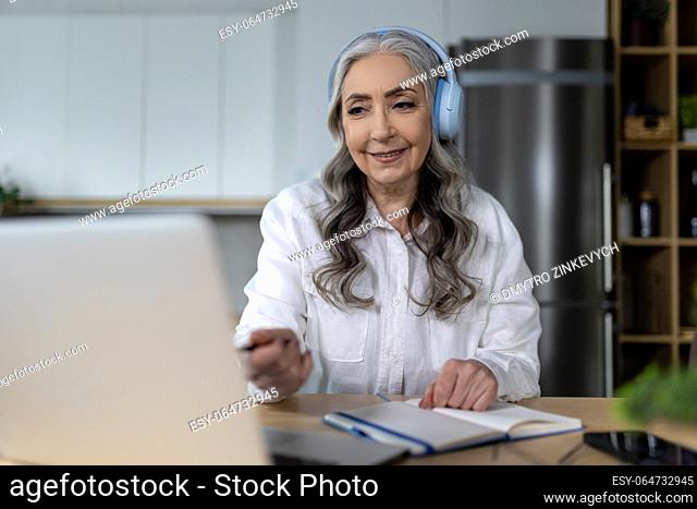 Online tutorial. Senior woman in headphones listening an online seminar