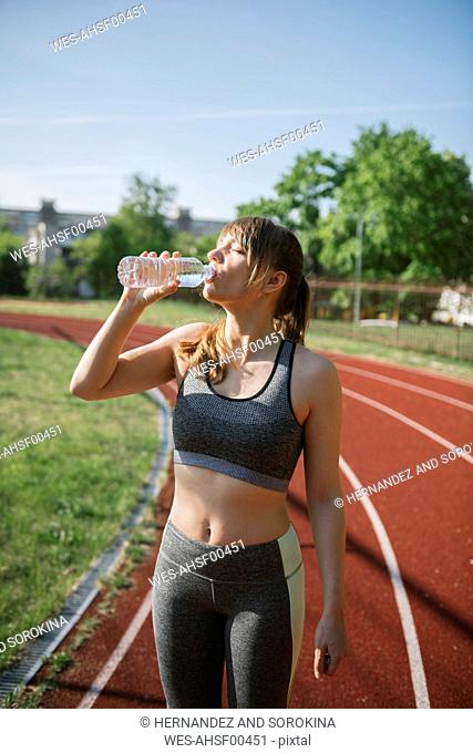 Sportswoman drinking water on racetrack