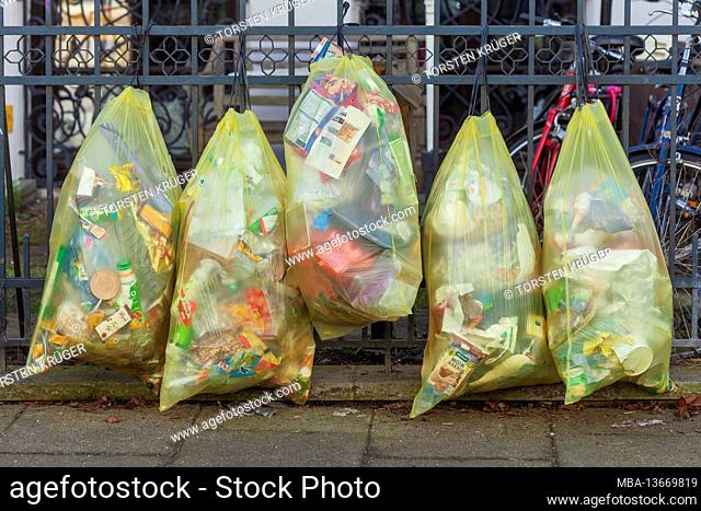 Yellow bags for plastic waste, hanging on a garden fence, Germany