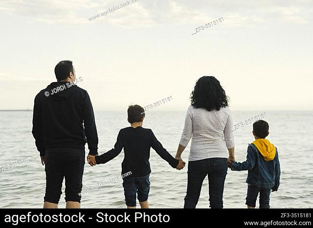 Family of four members standing on the beach and watching at the sea