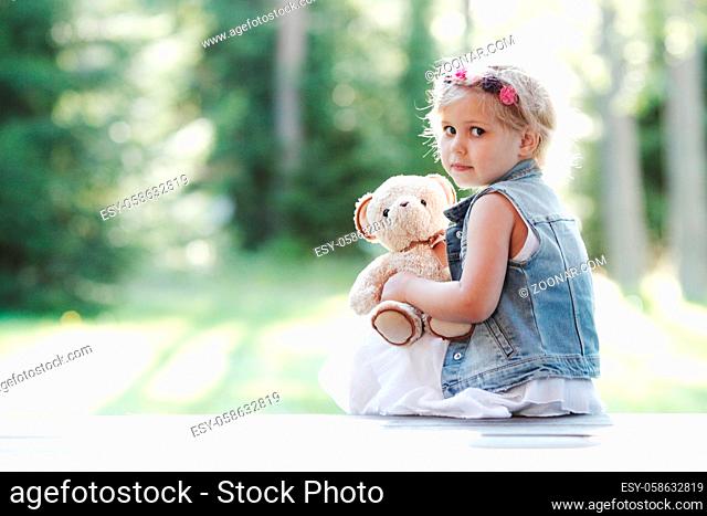 Worried Little girl holding her Teddy bear sitting outdoors