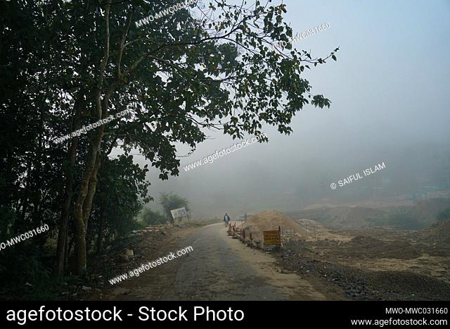 Man walking in the early dawn mist of a road that is under construction road along with a bridge in Bandarban, Chittagong, Bangladesh