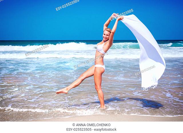Beautiful woman dancing on the beach wearing stylish swimsuit and holding white scarf, relaxation outdoors on tropical resort