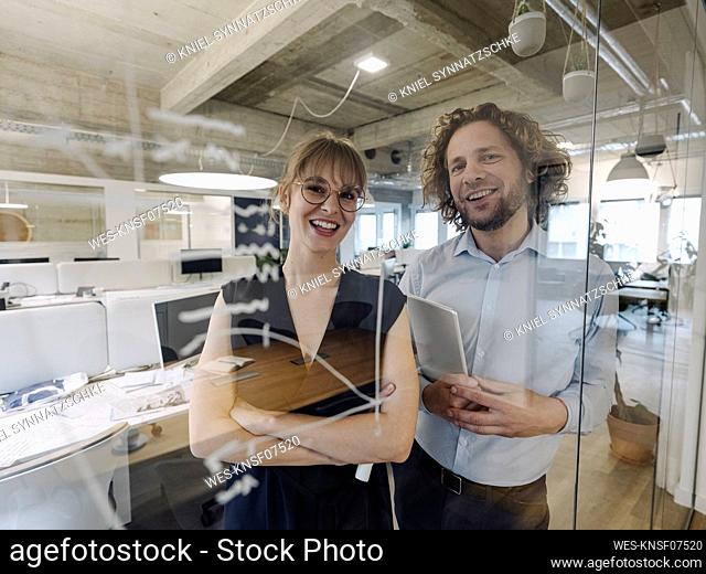 Portrait of happy businessman and businesswoman behind a glass pane in office