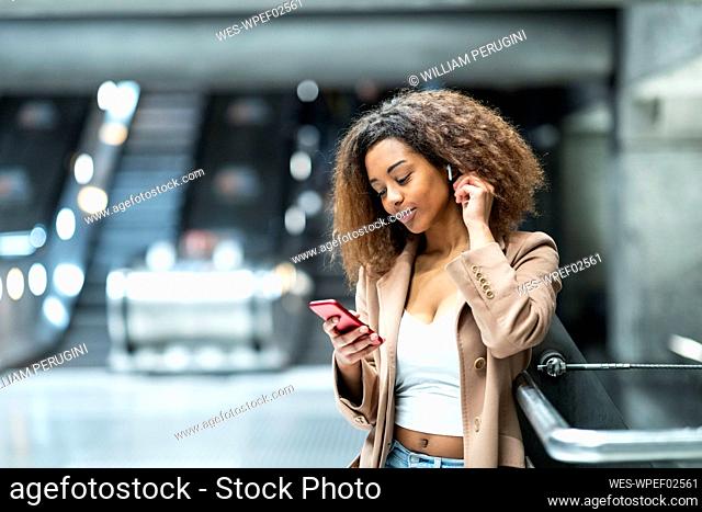 Young woman with cell phone and earbuds at subway station