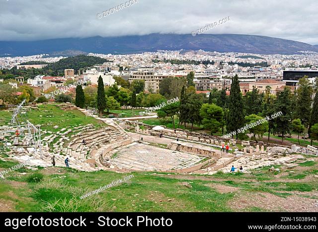 Athens, Greece - October 24, 2015: Ancient Greek ruins of Dionysus theatre, ruins amidst lush green grass. View from top of Acropolis in cloudy day