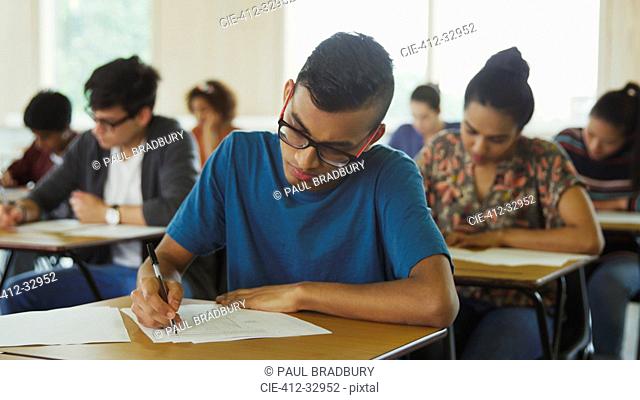 Male college student taking test at desk in classroom