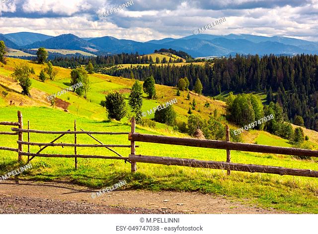 fence in front of a rural fields on hills. haystack on a grassy slope and mountain ridge in the distance