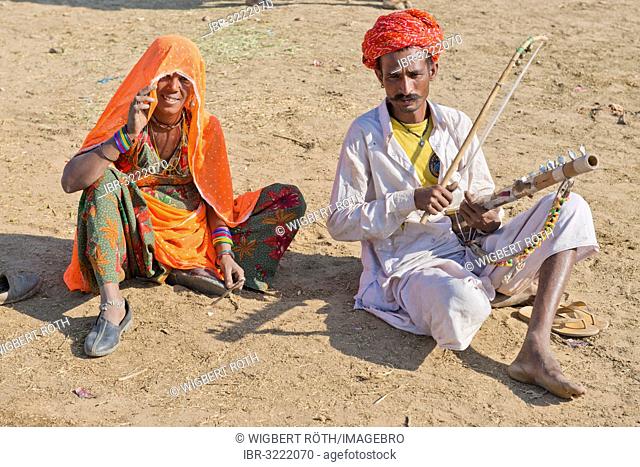 Indian men with a turban and wearing the traditional men's garment Dhoti, playing a sitar, woman with a colourful sari sitting next to him