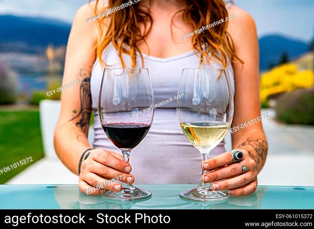 unrecognizable caucasian woman hands with tattoos on pair of red wine and white wine glasses, different wines tasting choosing comparison concept