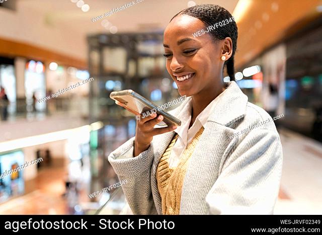 Happy girl talking on speaker of smart phone in shopping mall