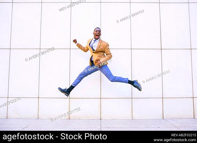 Young businessman jumping and shouting in front of a wall