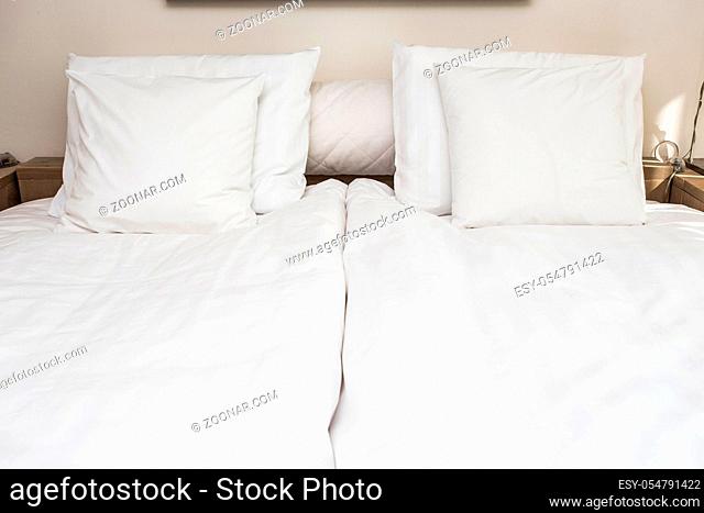 Bed maid-up with clean white pillows and bed sheets in beauty room. Close-up. Lens flair in sunlight. in a modern room