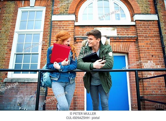 Young college student couple leaning against campus handrail chatting