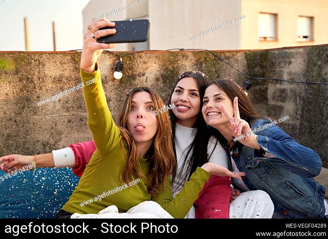 Happy female friends taking selfie through smart phone on rooftop