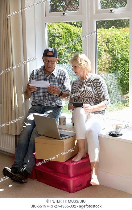 Moving house. Couple sitting on a window seat opening an account to be settled before completion of the sale