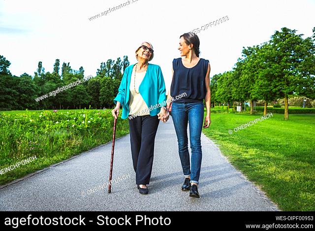Smiling grandmother holding hand of granddaughter while walking on road