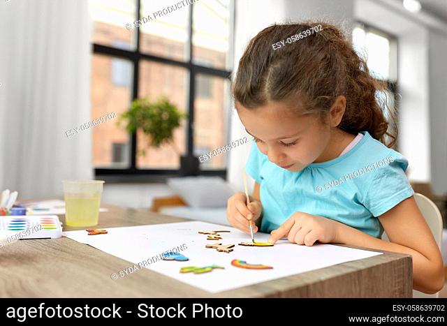 little girl painting wooden items at home