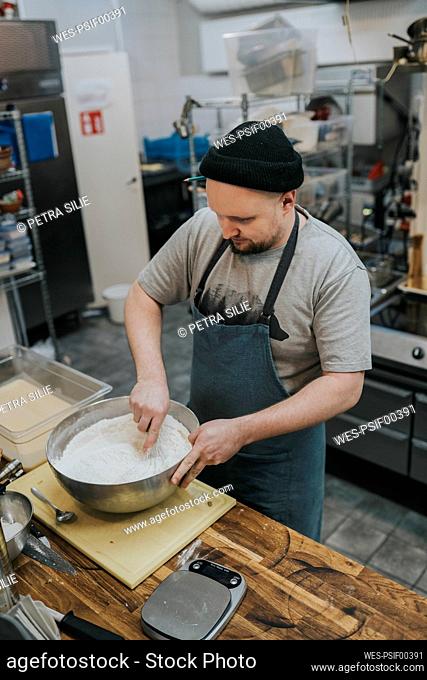 Male chef mixing flour in bowl at commercial kitchen counter
