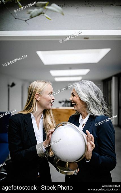 Happy mature and young businesswoman holding globe
