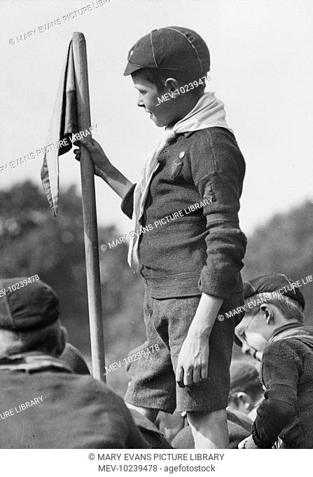 A wolf cub scout stands holding a flag at a scouting gathering at Hyde Park London held in the presence of Sir Robert Stephenson Smyth Baden Powell 1857-1941