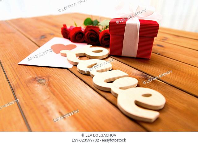 love, romance, valentines day and holidays concept - close up of gift box, red roses and greeting card with heart on wood