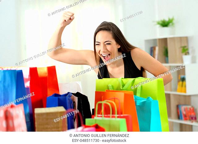 Excited woman looking at multiple colorful shopping bags at home
