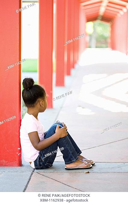 A mixed race little black girl quitely sits in a school yard