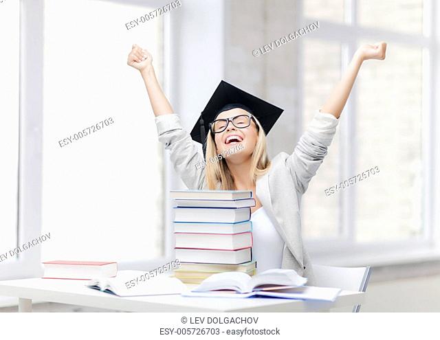happy student in graduation cap with stack of books