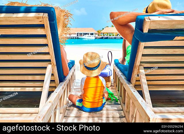 Family at beach on wooden sun bed loungers, young couple with three year old boy. Summer vacation at Maldives