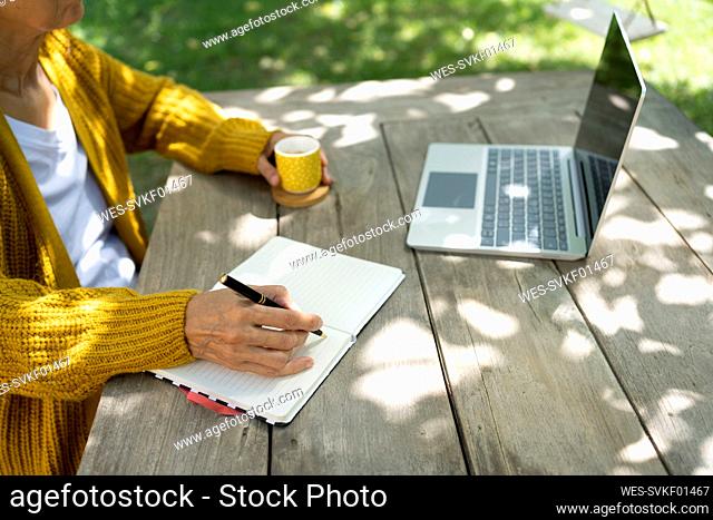 Female freelancer writing in diary and working on laptop at table