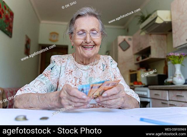 Happy senior woman counting paper currency at home