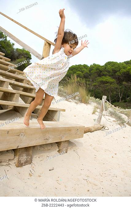 Almost 3 years old little girl jumping from a stair on a beach in Menorca, Spain