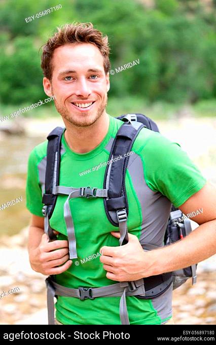 Active man portrait of sporty guy hiking outdoors. Young male hiker smiling happy at camera wearing backpack outdoors during hike in forest nature