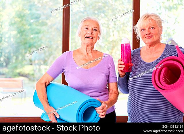 Zwei vitale Senior Frauen mit Yogamatte im Yogakurs im Fitnesscenter