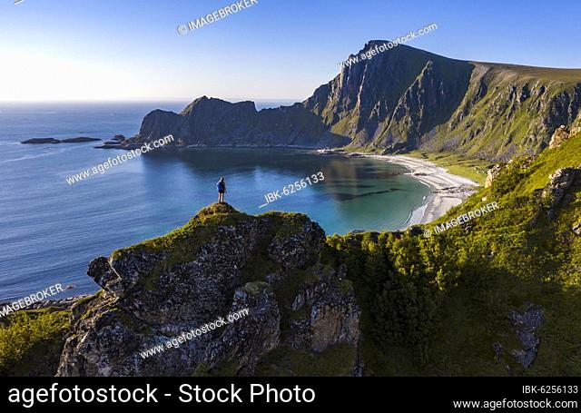 Hiker standing at the precipice, cliffs, beach and sea, in the back peak of the mountain Måtinden, near Stave, Nordland, Norway, Europe