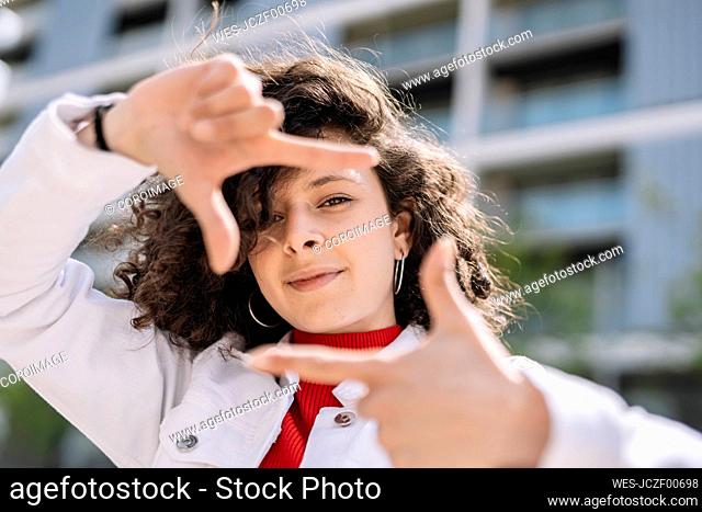 Young woman making finger frame with hands on sunny day