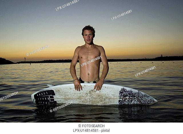 A young male surfer in the water after sunset