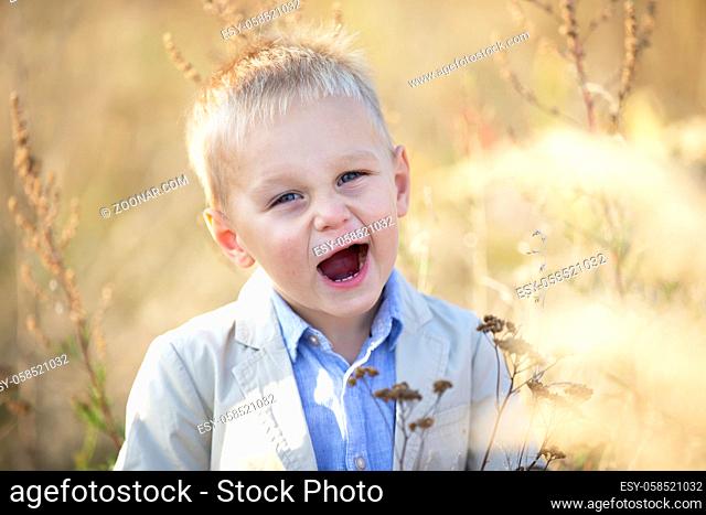 Funny cheerful little boy with blond hair smiles and looks into the camera