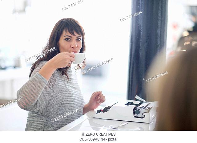 Mid adult woman drinking coffee with typewriter