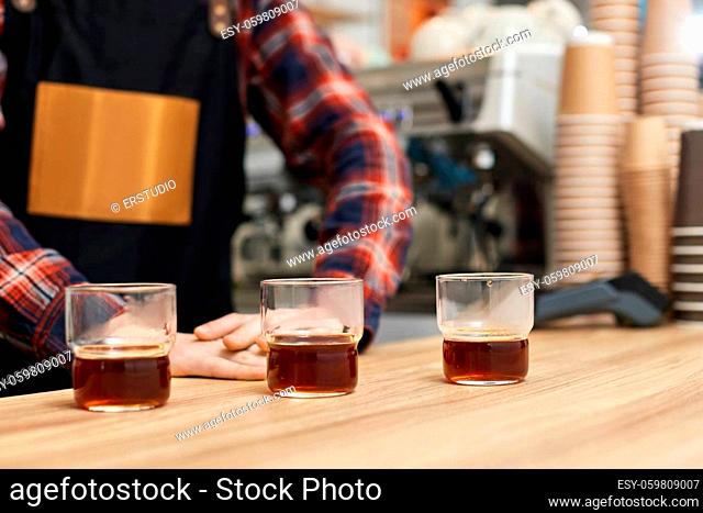 three glasses of freshly brewed coffee on wooden table and barista on background