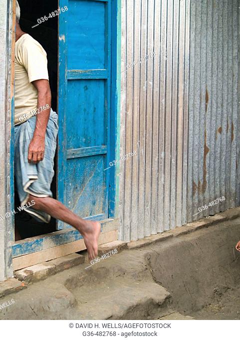 Villager enters mud floored house in rural Bangladesh