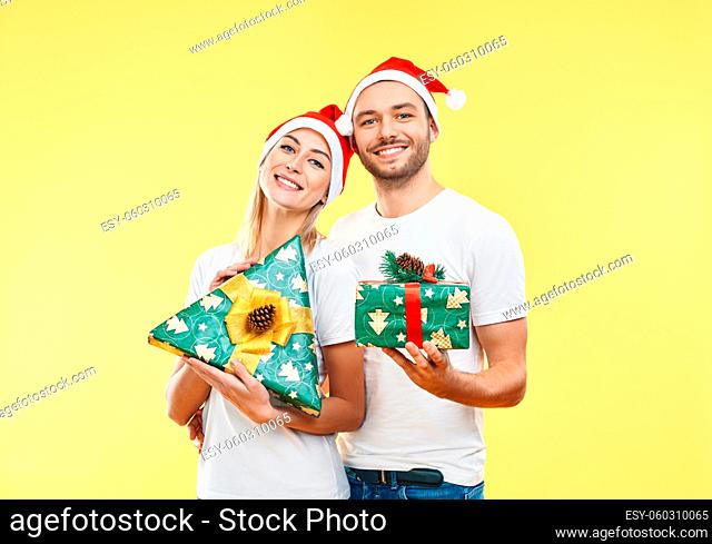 Young happy couple with xmas gift boxes over yellow background. Present, holiday, celebration concept