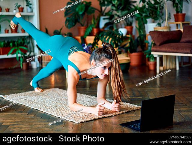 Young sporty woman doing yoga plank watching online exercises on her laptop. Healthy lifestyle concept