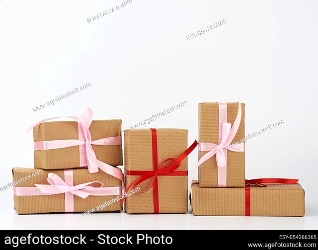 stack of gifts in boxes wrapped in brown kraft paper and tied with silk ribbon on a white background. Festive concept, copy space