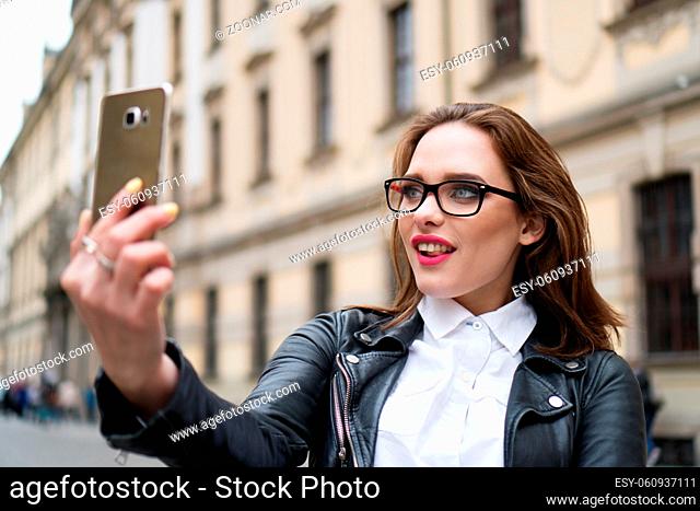 City lifestyle stylish hipster girl using a smartphone taking photo selfie with camera in a street