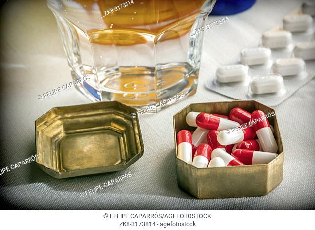 Old pillbox with capsules red and white next to a glass of water