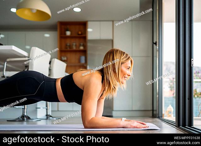 Female athlete looking through window while doing planks at home